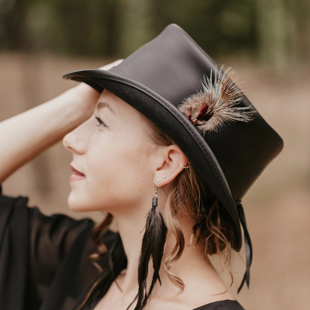 Woman wearing a black hat with feathers, standing outdoors.