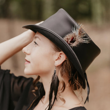 Woman wearing a black hat with feathers, standing outdoors.