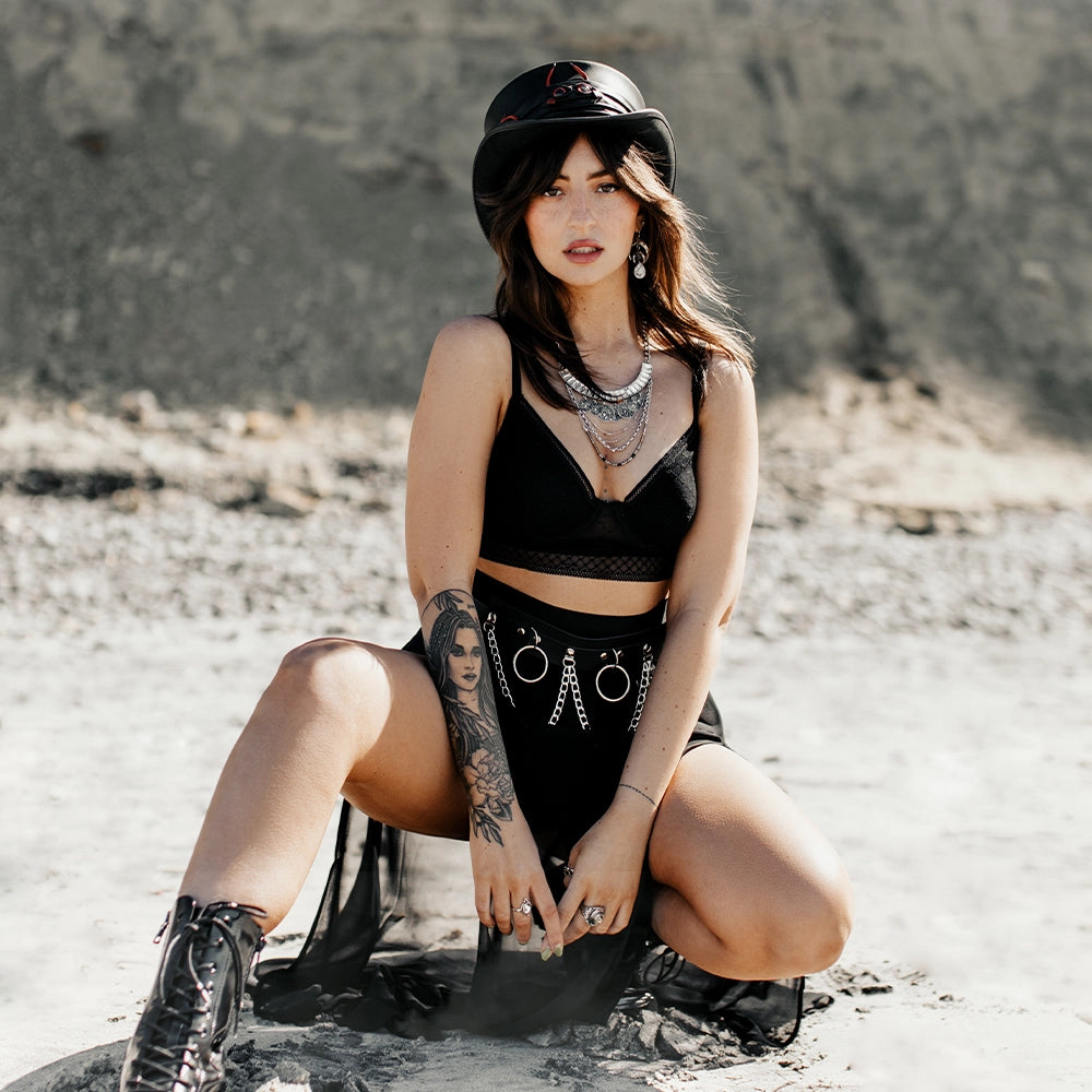 Woman in black outfit with tattoos sitting on a rock in a desert-like setting