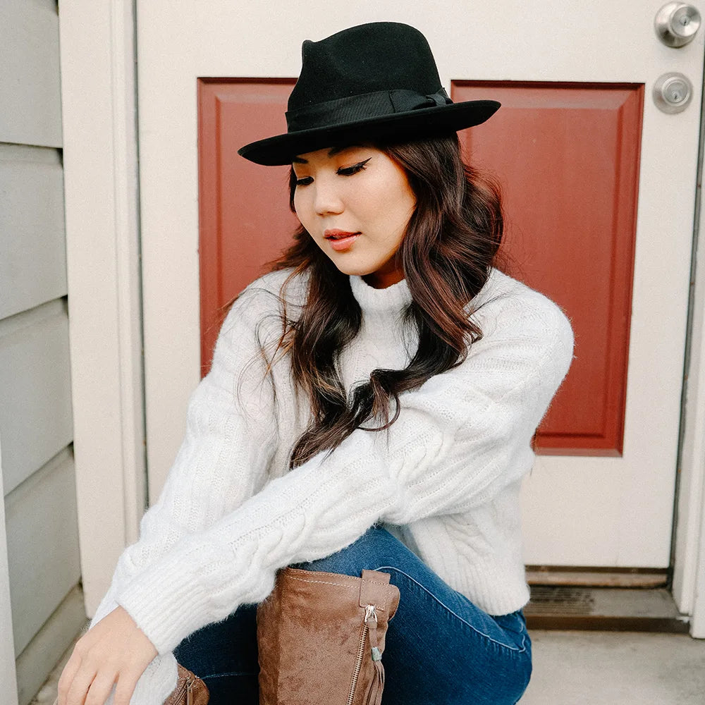 Woman wearing a black hat and white sweater sitting in front of a red door.