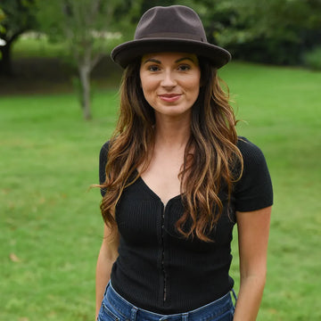 Woman wearing a black top and brown hat standing in a grassy area