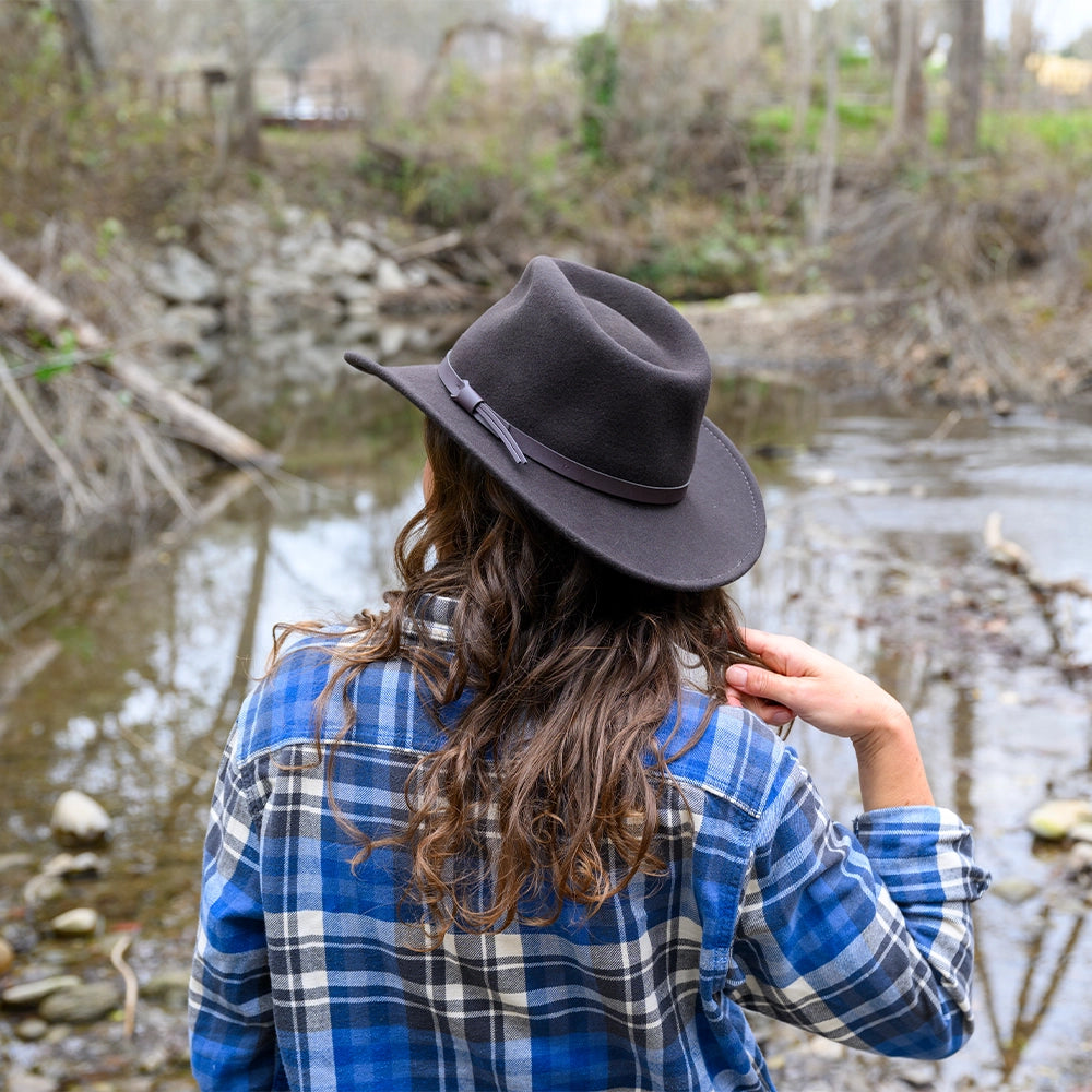 Person wearing a black hat and blue plaid shirt standing by a stream