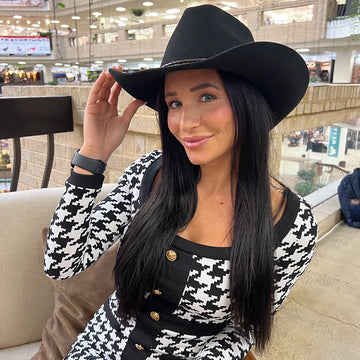 Woman wearing a black cowboy hat and a black and white patterned outfit in an indoor setting.