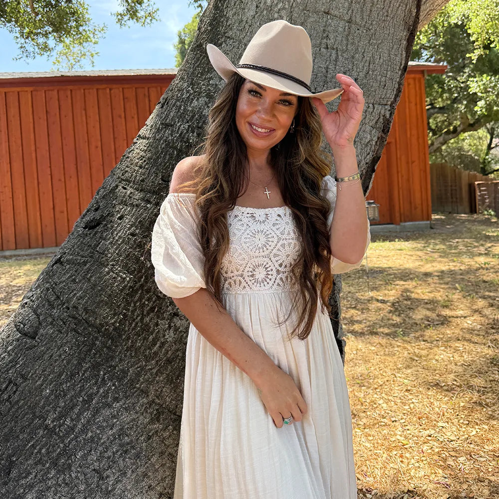 Woman in a white dress and beige hat standing next to a tree