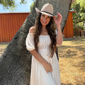 Woman in a white dress and beige hat standing next to a tree