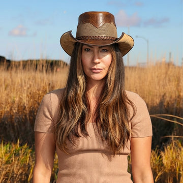 Woman wearing a brown cowboy hat in a field with a clear sky