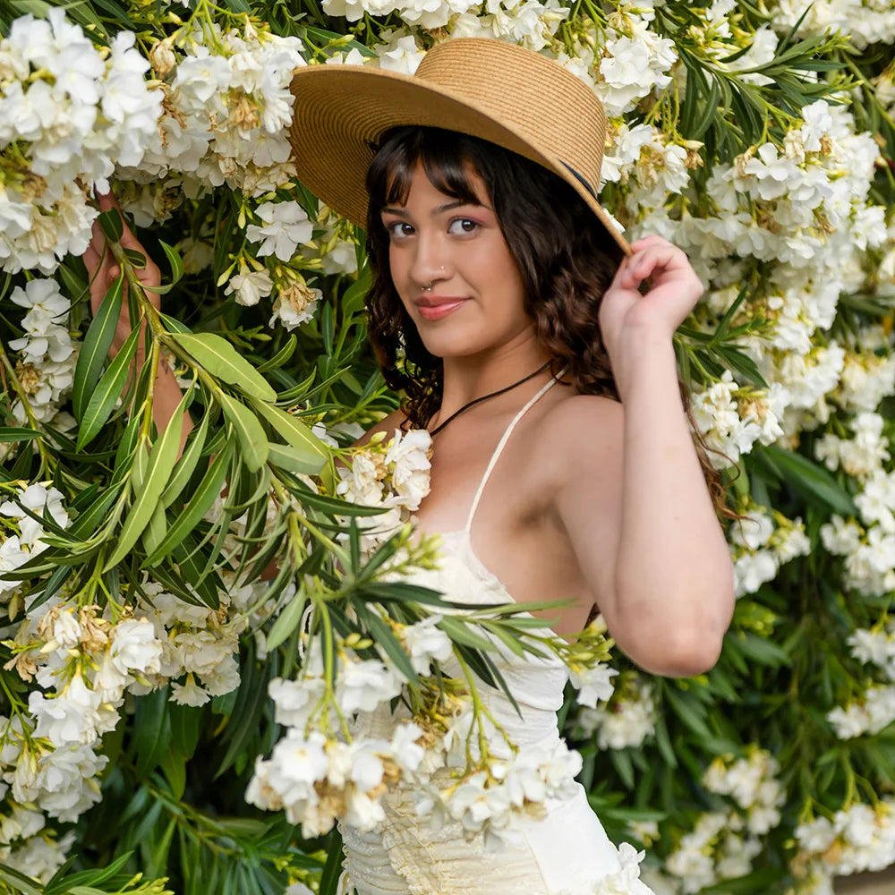 Woman in a white dress and straw hat standing among white flowers