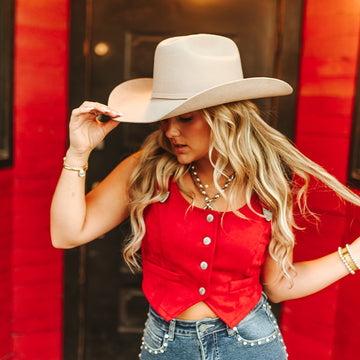 Woman wearing a red top and beige cowboy hat in front of a red wall.
