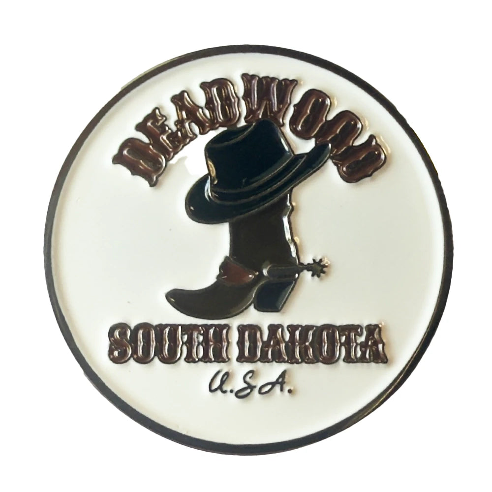A circular enamel pin featuring a black cowboy hat and boot with a spurs detail on a white background, with the text 'DEADWOOD SOUTH DAKOTA U.S.