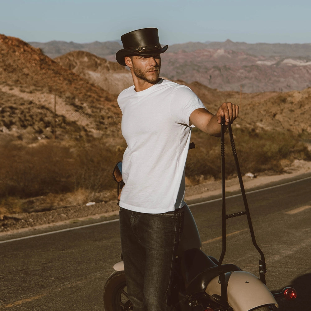 Man in a white t-shirt and black hat standing on a road with mountains in the background