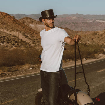 Man in a white t-shirt and black hat standing on a road with mountains in the background