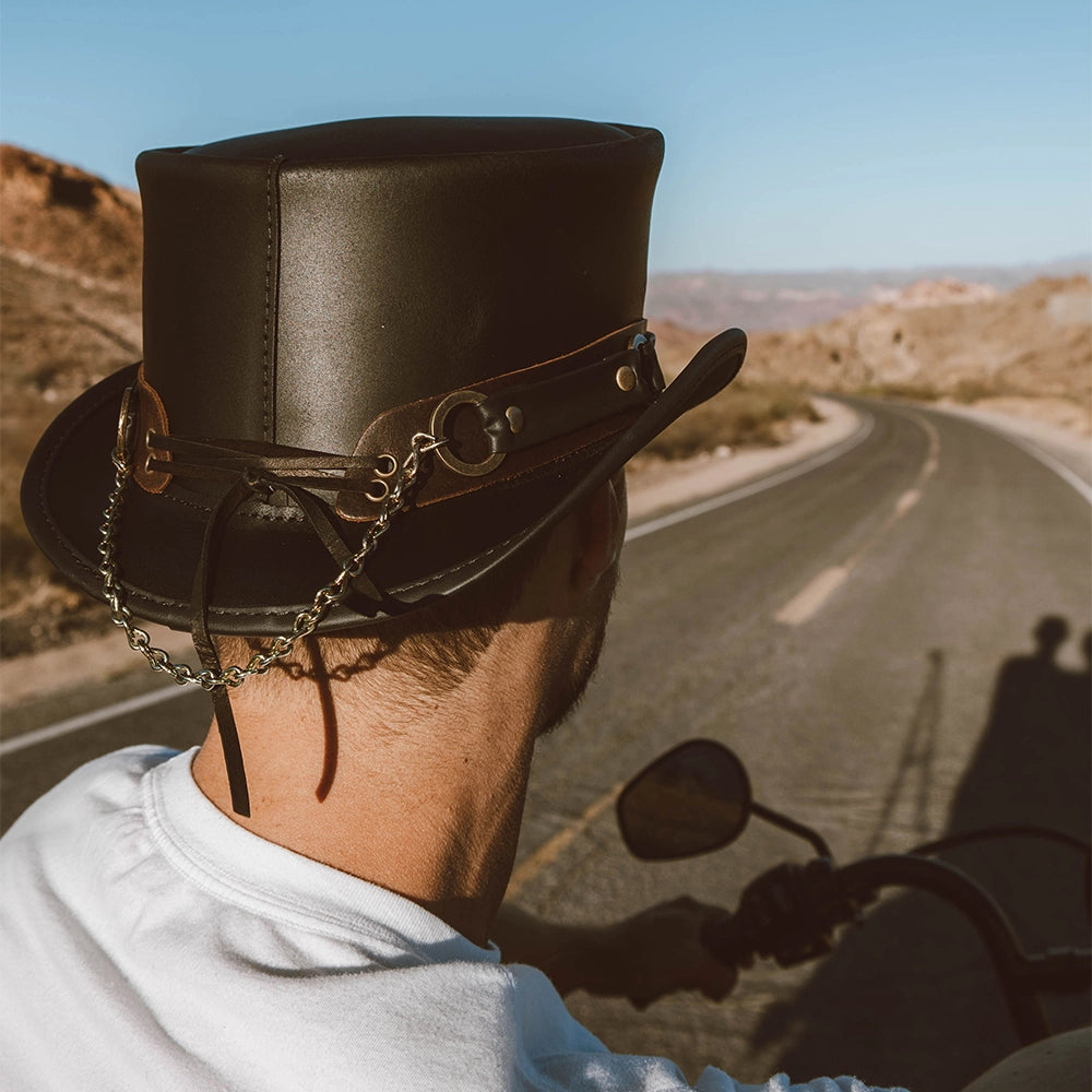 Person wearing a leather top hat on a motorcycle with a desert road in the background