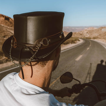 Person wearing a leather top hat on a motorcycle with a desert road in the background