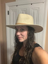A woman wearing a light beige woven cowboy hat, photographed in a selfie-style indoor portrait in front of a white paneled door.