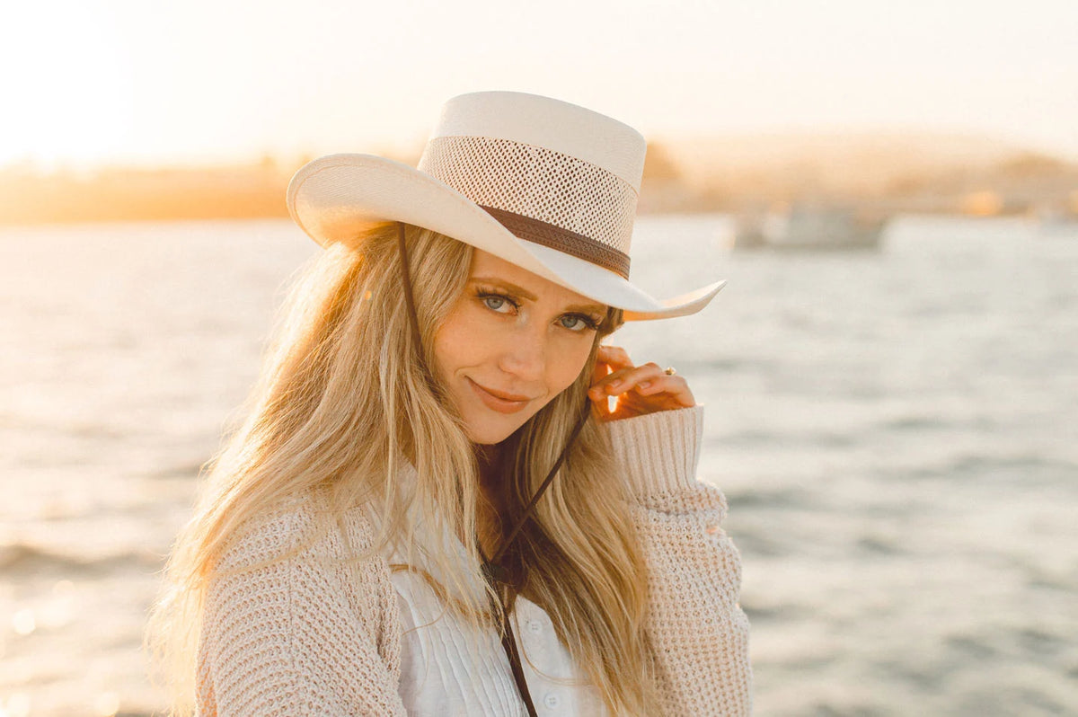 woman on a boat wearing a sweater at sunset and a american hat maker straw boater hat
