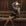Woman in black outfit and cowboy hat sitting on a wooden bench with a rustic background