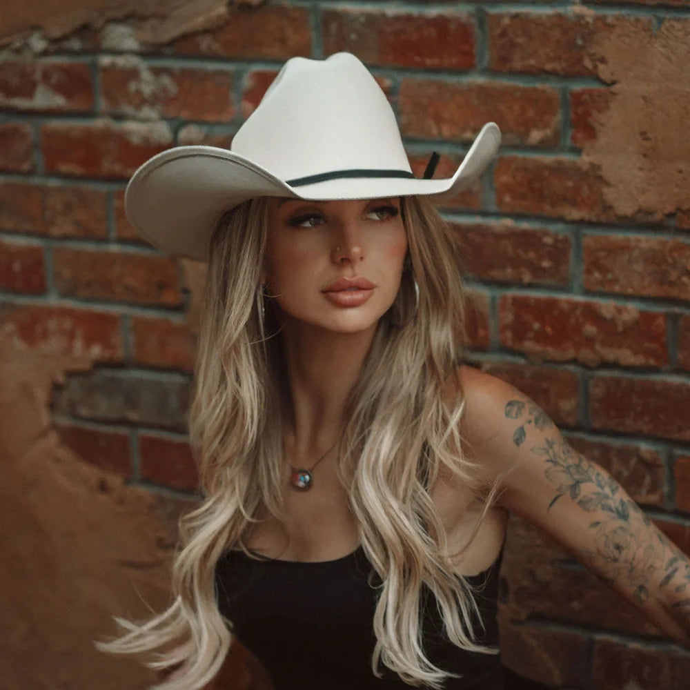 Woman wearing a white cowboy hat against a brick wall