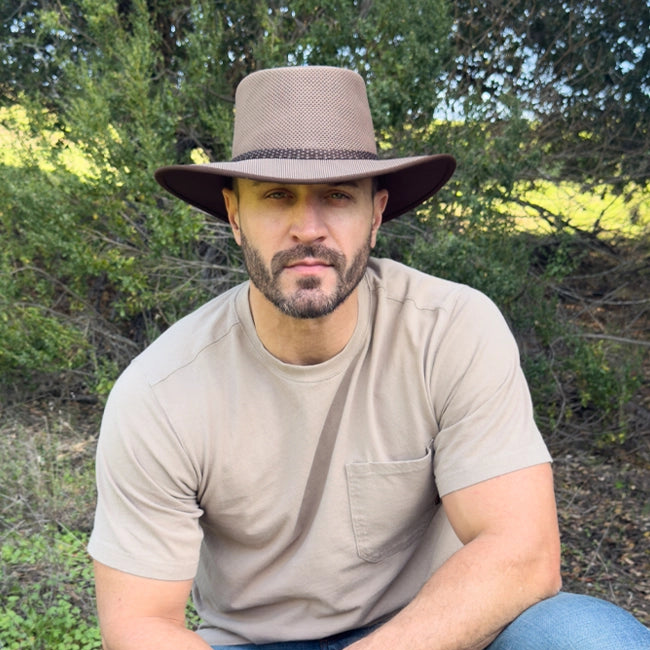 Man wearing a wide-brimmed hat sitting outdoors with trees in the background
