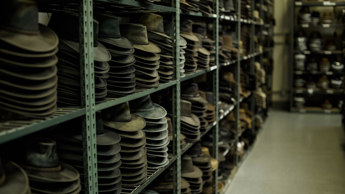 Rows of shelves filled with stacks of vintage dark hats in a storage room.